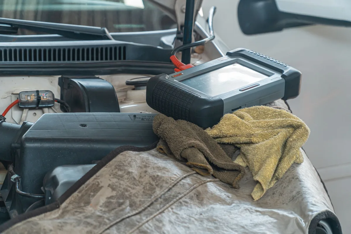 Mécanicien effectuant un diagnostic électronique sur une voiture dans un atelier professionnel.