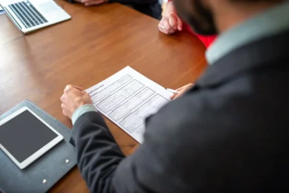Mains tenant un stylo sur un carnet ouvert à côté d'un ordinateur portable, dans un bureau calme