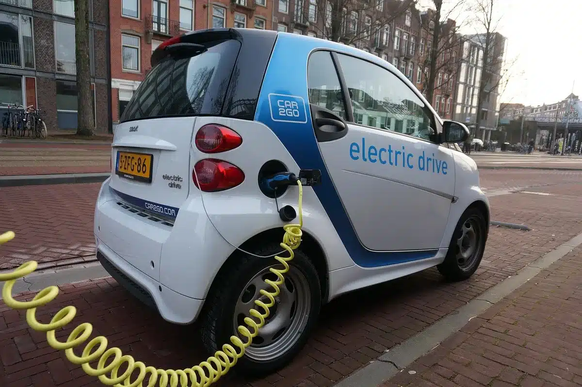 Câble de recharge branché sur une prise domestique à côté d'une voiture rechargeable