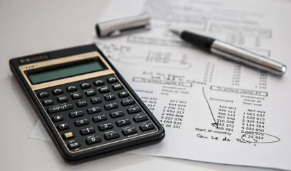 Mains d'une personne tenant des documents de rénovation énergétique et un calculatrice sur un bureau