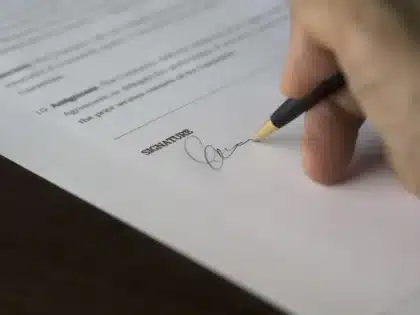Deux mains anonymes signant des papiers devant une voiture en plein jour