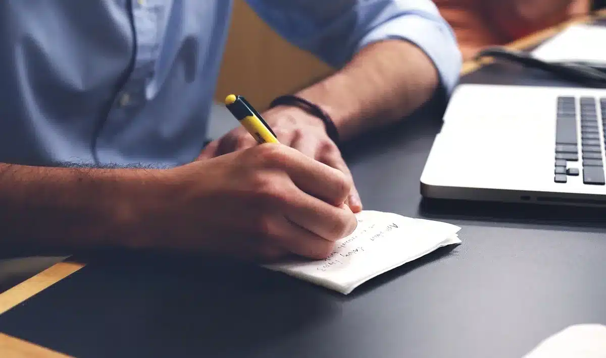 Mains prenant des notes dans un carnet sur un bureau ensoleillé