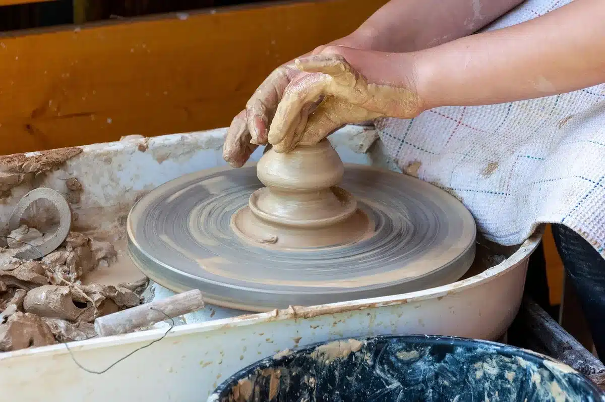 Atelier lumineux avec coquillages et mains d'artisan arrangeant une composition sur un panneau en bois