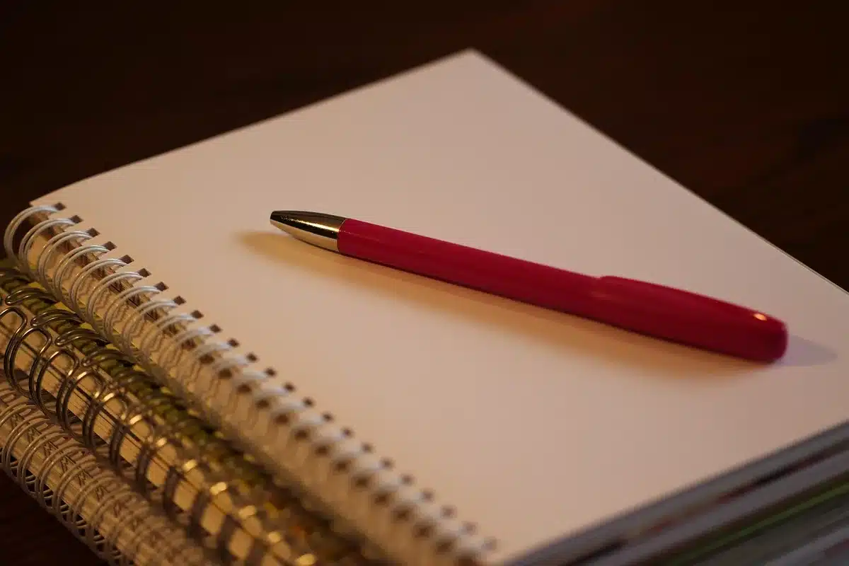 Personne prenant des notes sur un carnet dans un bureau lumineux avec ordinateur flou