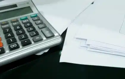 Mains anonymes sur une calculatrice et des tableaux financiers près d'une fenêtre en plein jour