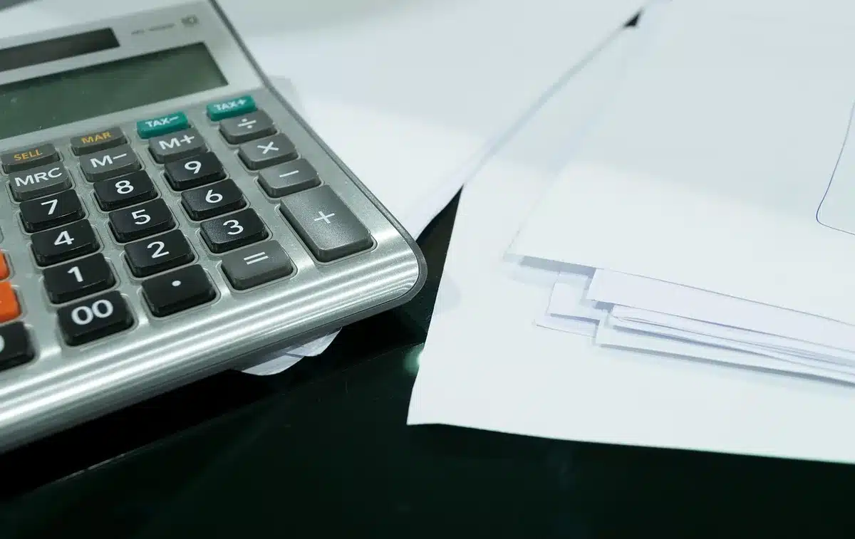 Mains anonymes sur une calculatrice et des tableaux financiers près d'une fenêtre en plein jour